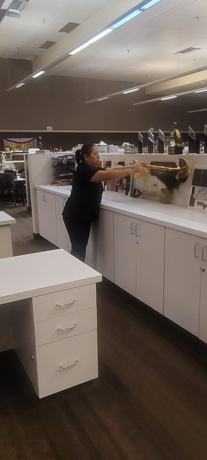 Woman cleaning a large trophy with a cloth in an office with white cabinets and a wooden floor.